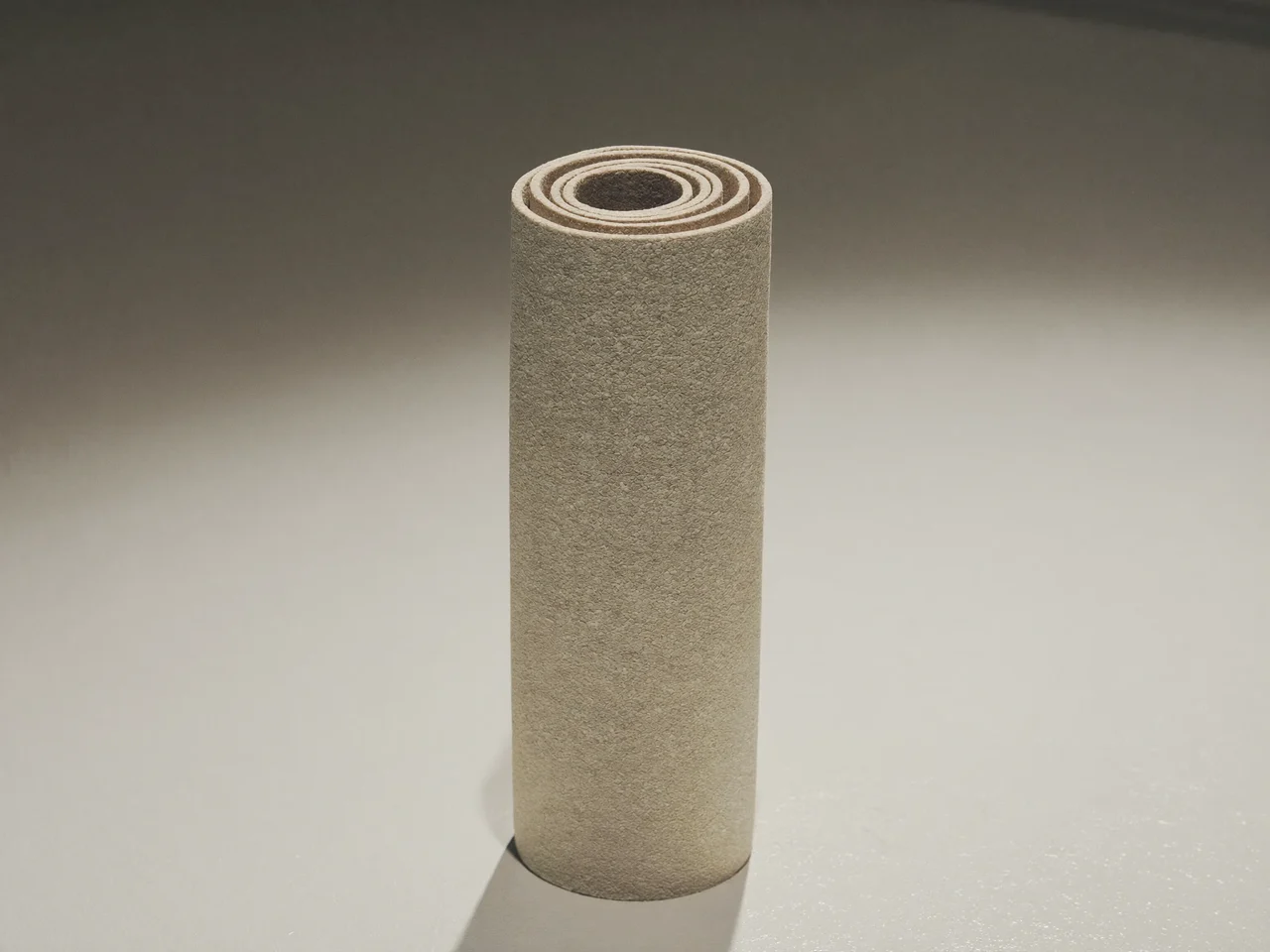 Tapis de yoga en caoutchouc naturel roulé, dressé sur une surface claire, grip texturé visible.