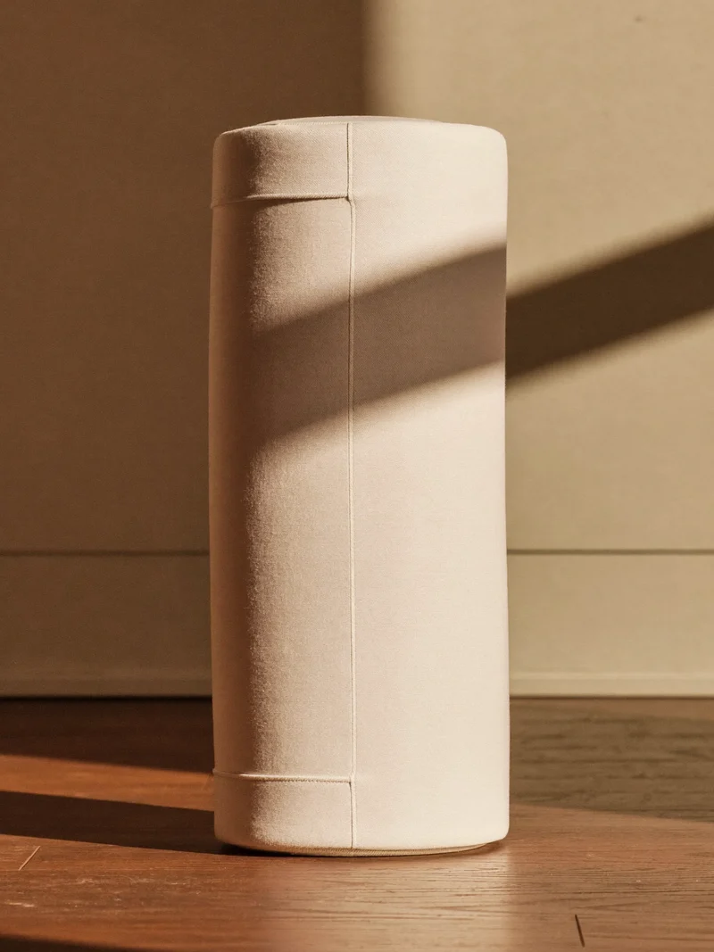 Bolster cylindrique en coton à housse tissée, appuyé contre un mur uni.